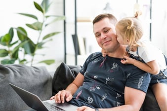little-girl-kissing-to-her-father-while-working-on-laptop_23-2147862326