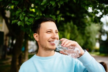 smiling-man-drinks-water-from-bottle-on-the-background-of-green-tree-in-summer-day_8353-7016